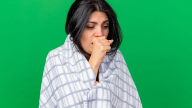 Mulher com tosse, coberta com um lençol xadrez, aparentando estar doente e desconfortável.