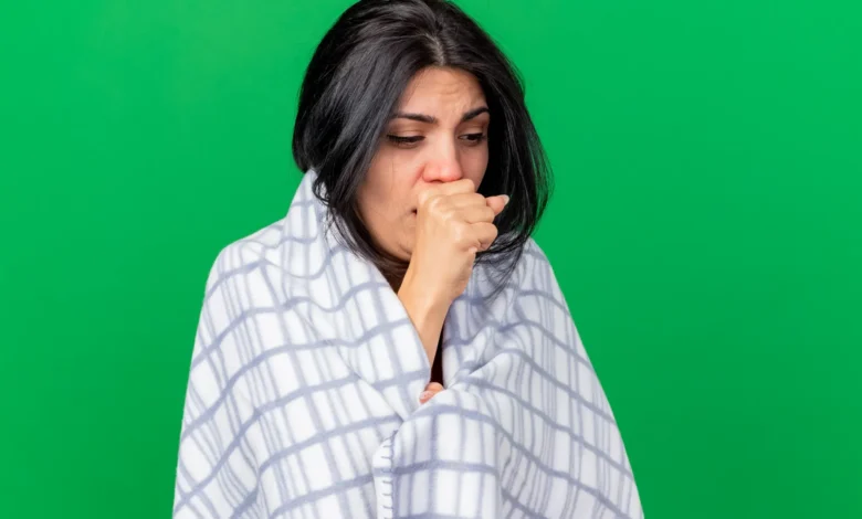 Mulher com tosse, coberta com um lençol xadrez, aparentando estar doente e desconfortável.