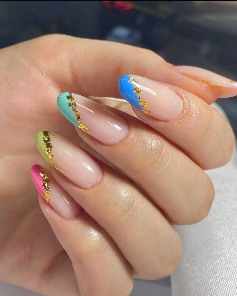 Nail art em tons pastel com detalhes dourados, incluindo verde, azul, rosa e dourado nas pontas das unhas.