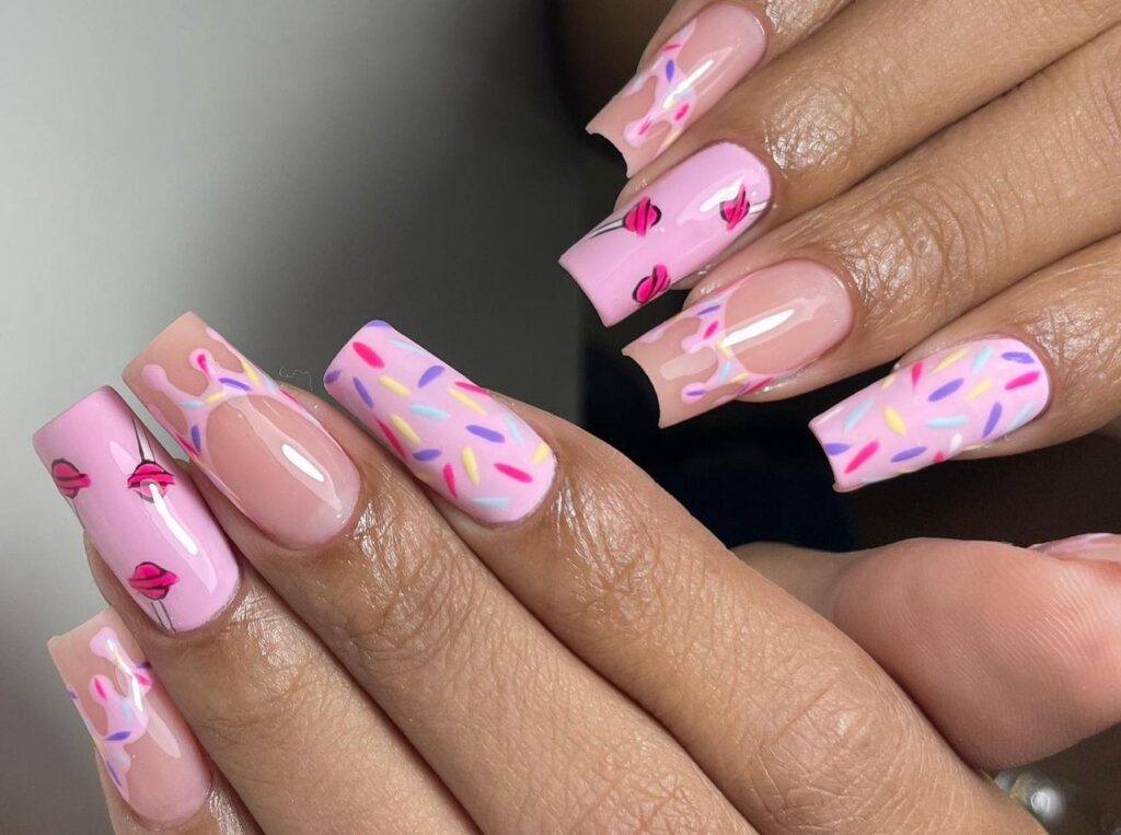 Unhas decoradas com desenhos de doces, incluindo confeitos e glacê, no estilo de nail art japonesa delicada.