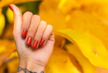 Mão feminina com esmalte vermelho e fundo de folhas amarelas vibrantes