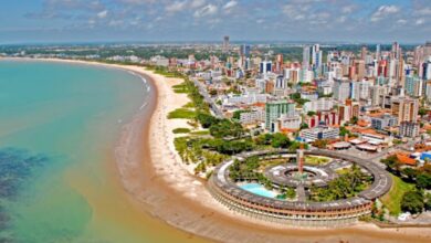 Vista aérea de cidade litorânea no Nordeste com orla urbanizada e prédios modernos.