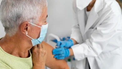 Idosa recebendo vacina contra doenças em uma clínica de saúde com a ajuda de um profissional médico usando máscara e luvas.
