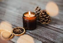 Vela aromática com rodelas de laranja seca e pinhas sobre madeira rústica
