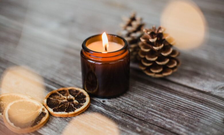 Vela aromática com rodelas de laranja seca e pinhas sobre madeira rústica