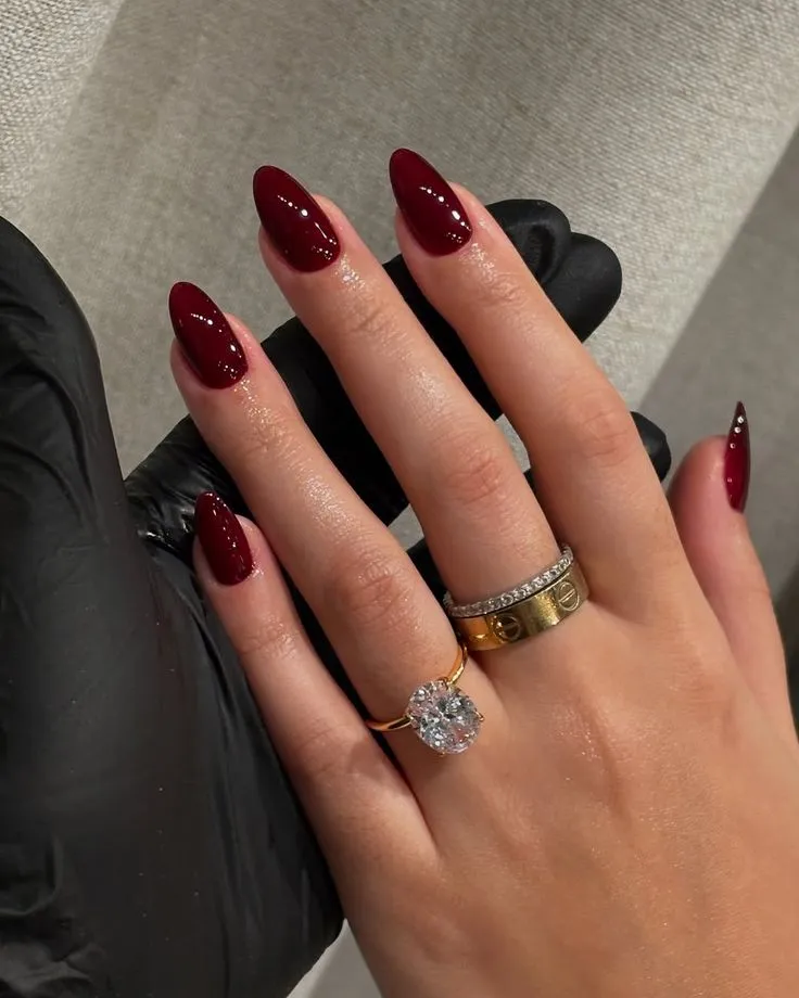 Unhas vermelhas escuras, um símbolo de elegância e poder, com anéis sofisticados.