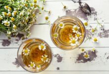 Xícaras de chá de camomila com flores naturais sobre mesa de madeira