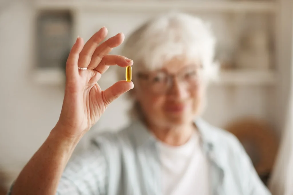 Mulher idosa segurando cápsula de óleo de peixe, um suplemento de ômega-3, essencial para equilibrar a vitamina D.