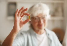 Mulher idosa segurando cápsula de óleo de peixe, um suplemento de ômega-3, essencial para equilibrar a vitamina D.