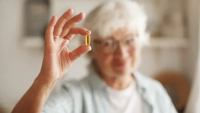 Mulher idosa segurando cápsula de óleo de peixe, um suplemento de ômega-3, essencial para equilibrar a vitamina D.