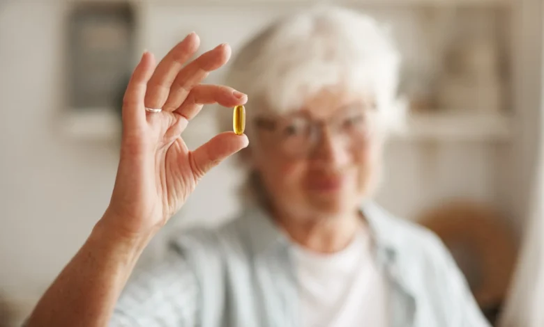 Mulher idosa segurando cápsula de óleo de peixe, um suplemento de ômega-3, essencial para equilibrar a vitamina D.