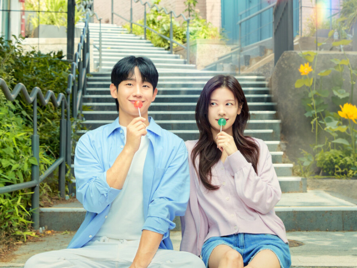 Doramas. Casal sorridente, um homem e uma mulher jovens asiáticos, sentados em uma escadaria externa, ambos segurando pirulitos.