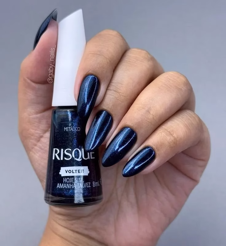 Unhas com esmalte metálico azul escuro brilhante, da marca Risqué, com o título 'Voltei!