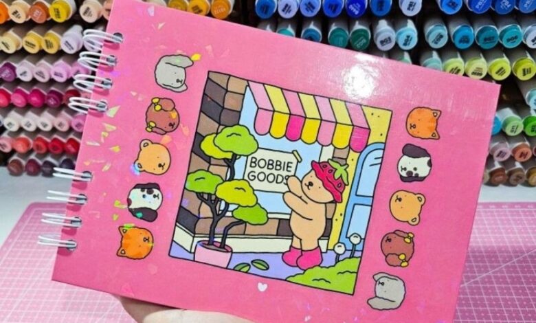 Caderno com ilustração de canetinhas Bobbie Goods e personagem com fantasia de morango, ilustrando um cenário de loja.