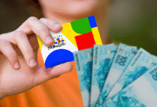 A mão de uma pessoa segura o cartão do Bolsa Família e algumas notas de 100 reais, com foco nos detalhes dos documentos.