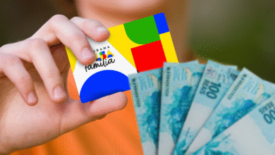 A mão de uma pessoa segura o cartão do Bolsa Família e algumas notas de 100 reais, com foco nos detalhes dos documentos.