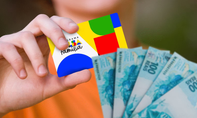 Cartão do Bolsa Família segurado por uma mão ao lado de cédulas de 100 reais