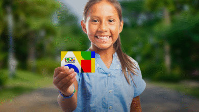 Criança segurando o cartão do Bolsa Família com sorriso, em um ambiente ao ar livre.