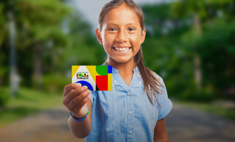 Criança segurando o cartão do Bolsa Família com sorriso, em um ambiente ao ar livre.