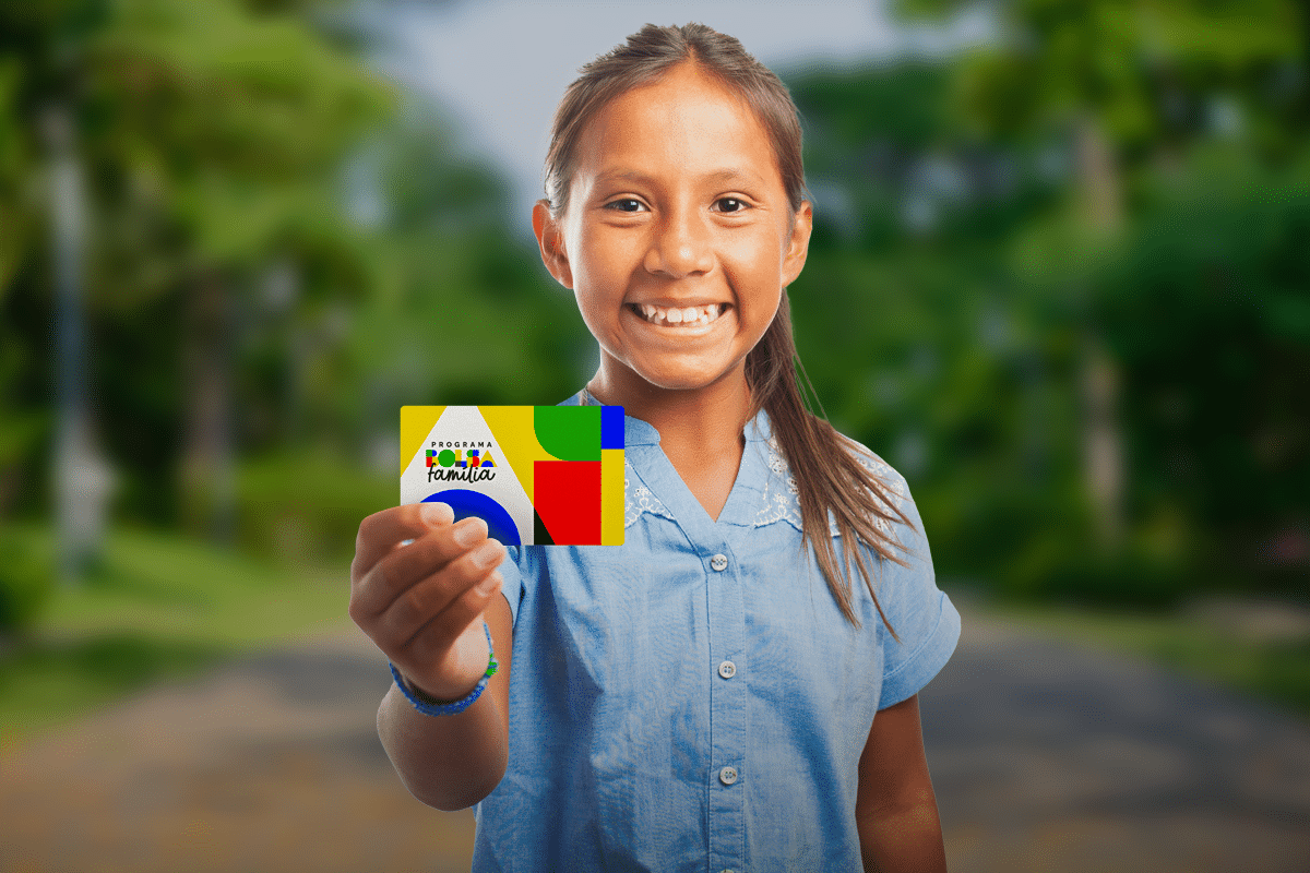 Criança segurando o cartão do Bolsa Família com sorriso, em um ambiente ao ar livre.