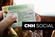 Imagem de uma carteira de habilitação brasileira sendo segurada, com uma mão em destaque, enquanto o motorista está no banco do passageiro de um carro. O tema é sobre a CNH Social 2025.