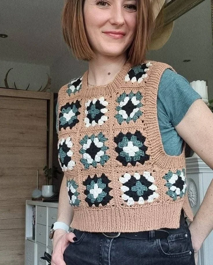 Imagem de um colete de crochê estilo granny square com quadrados em tons de verde, preto e branco, sobre fundo bege.