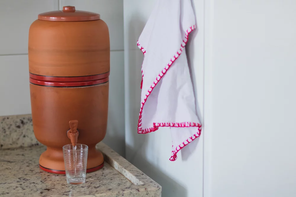 A Ciência por Trás do Filtro de Barro Filtro de barro sobre a bancada da cozinha, com um copo de água ao lado.