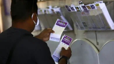 Loteria da Lotofácil da Independência 2025 sendo apostada por um homem, com bilhetes visíveis de diferentes jogos ao fundo.