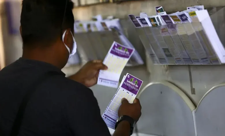 Loteria da Lotofácil da Independência 2025 sendo apostada por um homem, com bilhetes visíveis de diferentes jogos ao fundo.