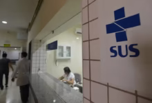Entrada do atendimento SUS com uma recepcionista no balcão e pessoas na área de espera.