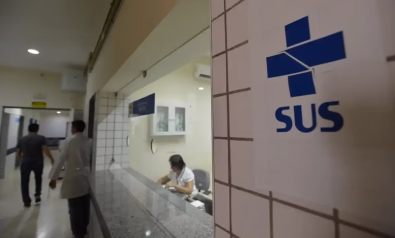 Entrada do atendimento SUS com uma recepcionista no balcão e pessoas na área de espera.