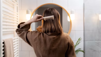 Pessoa penteando o cabelo para trás em um ambiente de banheiro moderno, refletida em um espelho redondo.