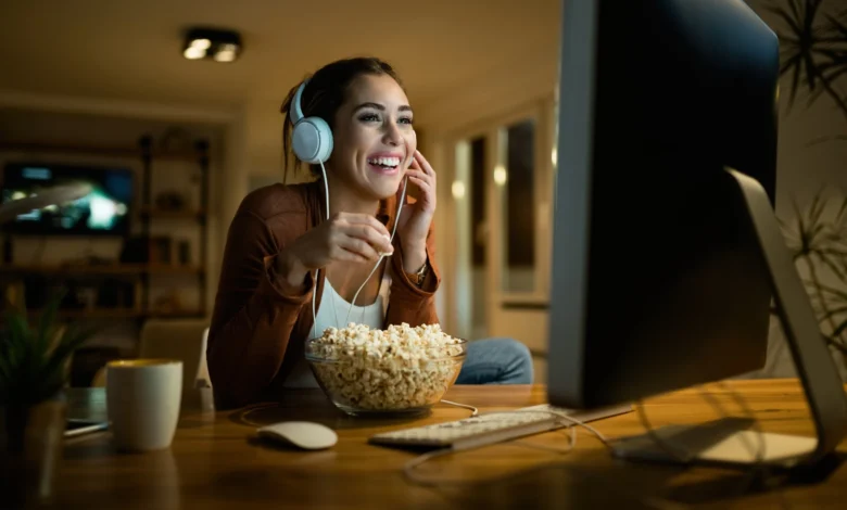 Mulher sorridente com fones de ouvido assiste a novela online enquanto come pipoca.