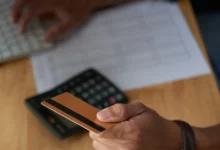 Homem segurando cartão de crédito com foco em mãos, teclado e calculadora ao fundo, simbolizando a gestão de pagamentos e faturas.