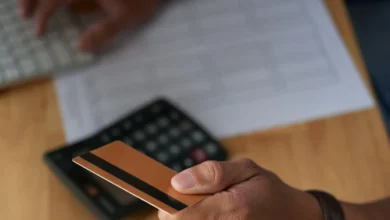 Homem segurando cartão de crédito com foco em mãos, teclado e calculadora ao fundo, simbolizando a gestão de pagamentos e faturas.