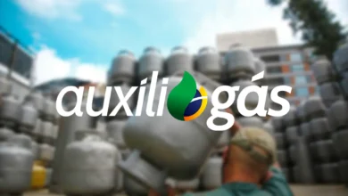 Homem carrega botijão de gás próximo a pilha de cilindros, com o logo do Auxílio Gás em destaque.
