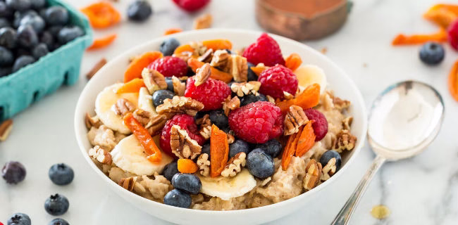 Mingau de aveia com frutas frescas, como framboesas, bananas, mirtilos e pedaços de cenoura.