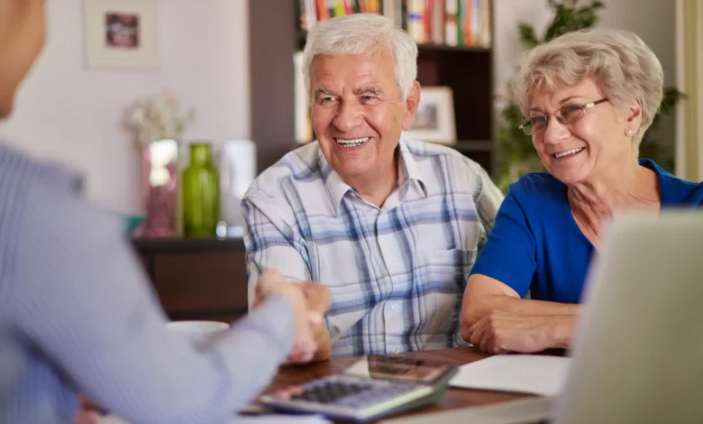 Imagem de um casal idoso sorrindo e apertando a mĂŁo de um consultor durante uma reuniĂŁo sobre previdĂȘncia privada.