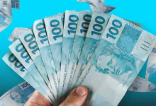 Imagem de várias cédulas de R$ 100, com foco em uma mão segurando uma pilha, simbolizando o pagamento do Bolsa Família e a consulta pelo Caixa Tem.