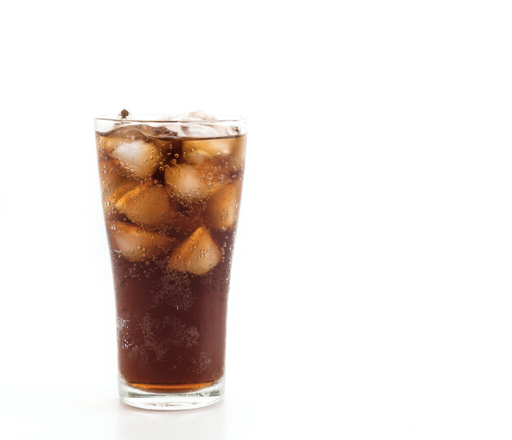Um copo de refrigerante com gelo sobre uma superfície branca, com o líquido e as bolhas visíveis.