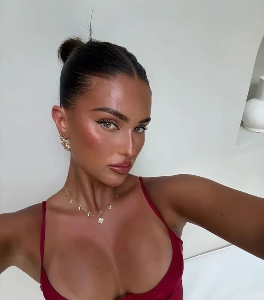 Mulher com coque moderno, maquiagem natural e usando acessórios delicados.