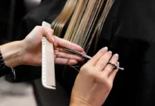 Profissional cortando cabelo em salão, com tesoura e pente, representando o processo de cortar para disfarçar a papada.