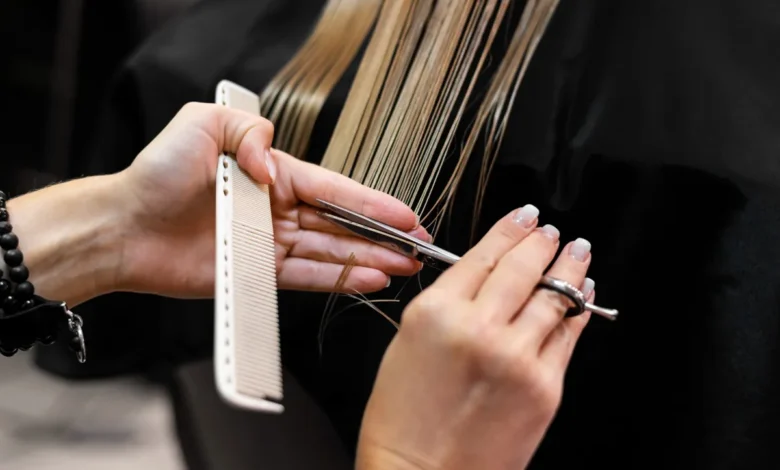 Profissional cortando cabelo em salão, com tesoura e pente, representando o processo de cortar para disfarçar a papada.