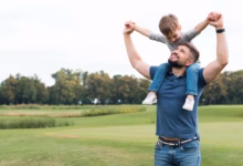 Pai segurando seu filho nos ombros em um campo aberto, ambos sorrindo, representando momentos de afeto e diversão no Dia dos Pais.