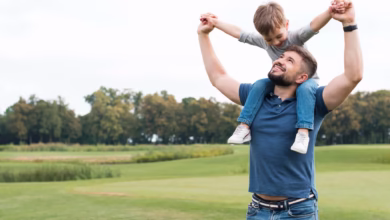 Pai segurando seu filho nos ombros em um campo aberto, ambos sorrindo, representando momentos de afeto e diversão no Dia dos Pais.