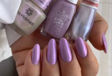 Unhas esmaltadas em tom lilás espelhado com três vidrinhos de esmalte ao fundo