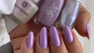 Unhas esmaltadas em tom lilás espelhado com três vidrinhos de esmalte ao fundo