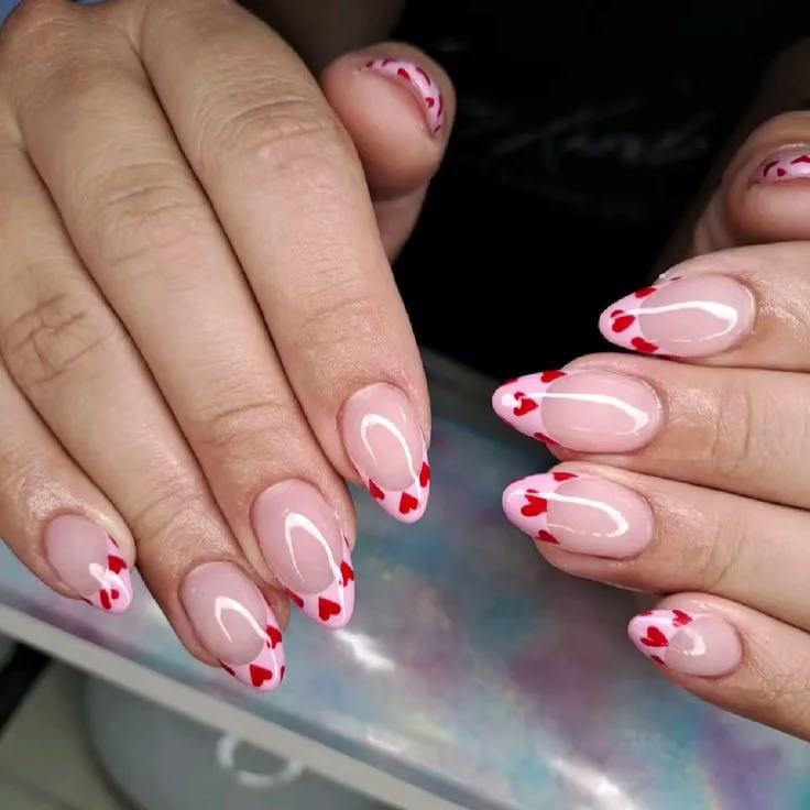Unhas com francesinha decorada com corações vermelhos e linhas brancas.