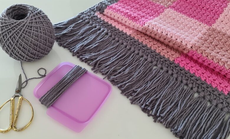 Acessórios e materiais para crochê, incluindo um novelo de lã cinza, tesoura e uma peça de crochê rosa, prontos para a confecção de um tapete.