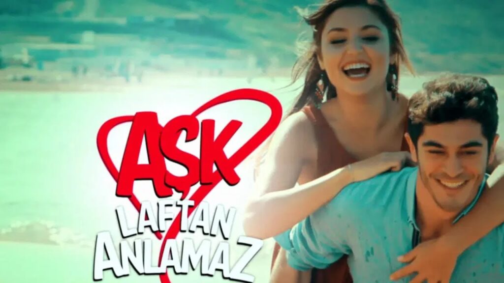 A imagem do casal principal da novela turca 'Aşk Laftan Anlamaz', se divertindo em um dia de sol, com o título da novela em primeiro plano.